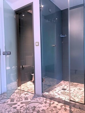 Een moderne badkamer met een douchecabine van glas, vloertegels met een patroon en een zichtbaar toilet.