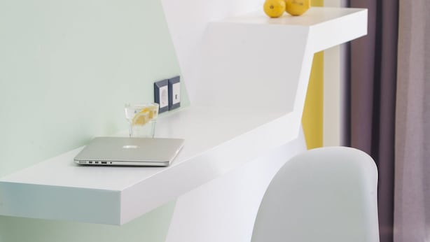 Ein modernes Zimmer mit einem weißen Stuhl, einem weißen Schreibtisch und einem weißen Regal mit zwei gelben Gegenständen.