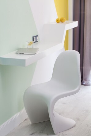 A modern room with a white chair, a white desk, and a white shelf with two yellow objects. - Blue Bottle Hotel (Thessaloniki)