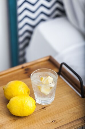 Una bandeja de madera con dos limones y un vaso de agua con cubitos de hielo.