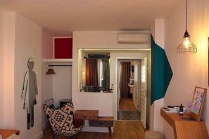 Een ruimtelijk ingerichte leefruimte met een spiegelwand, een gestreept fauteuil, een houten bankje en een bureau met een lamp.