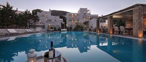 A poolside setting with a clear view of a building, outdoor seating, and a tray with a bottle and glasses.