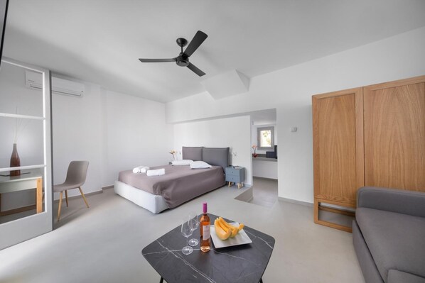 A modern hotel room with a bed, a desk, a chair, a dining table with a bottle and glasses, and a wardrobe.