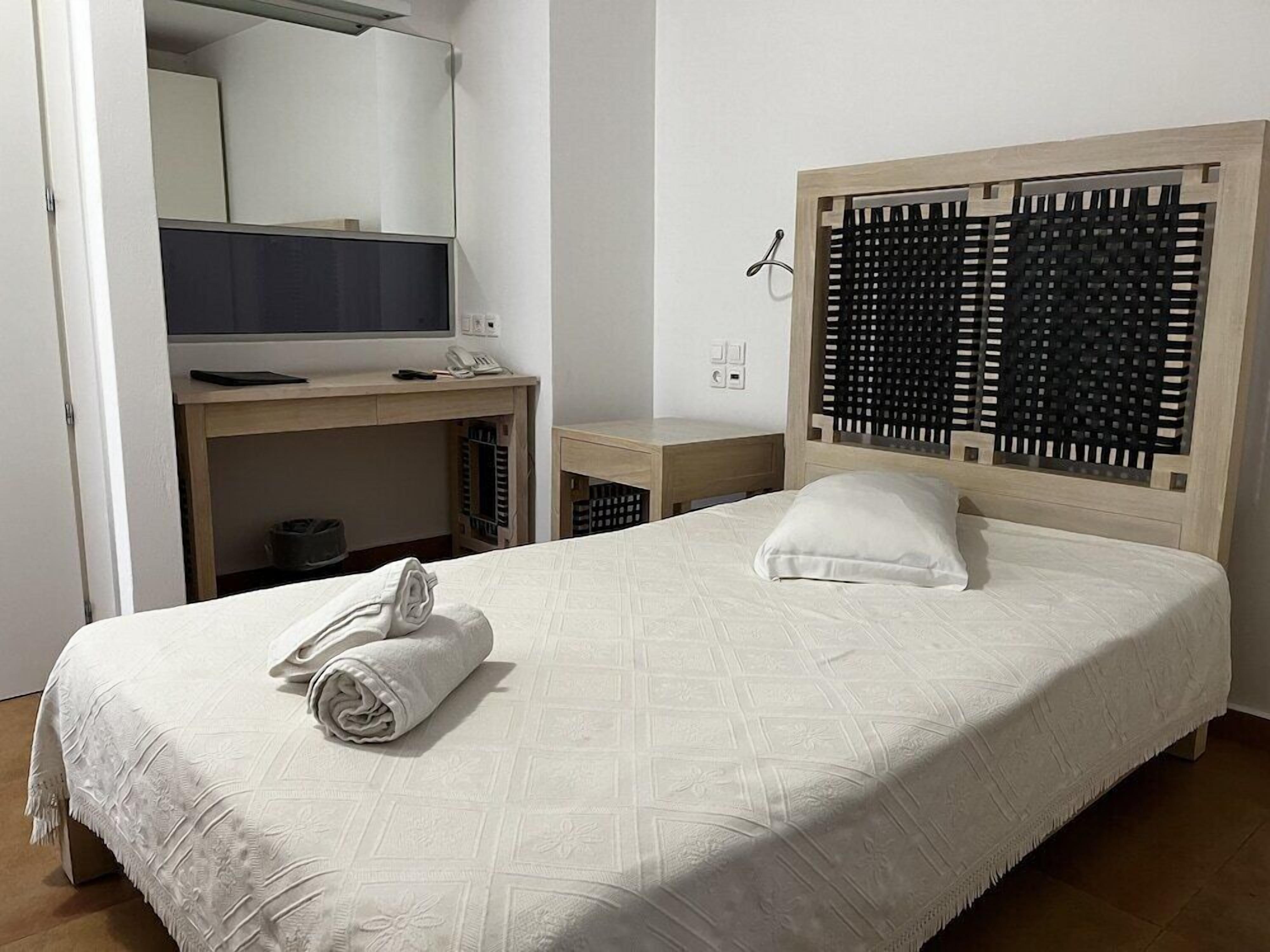 Une chambre d’hôtel avec un lit, un bureau, une chaise, un miroir et une fenêtre.