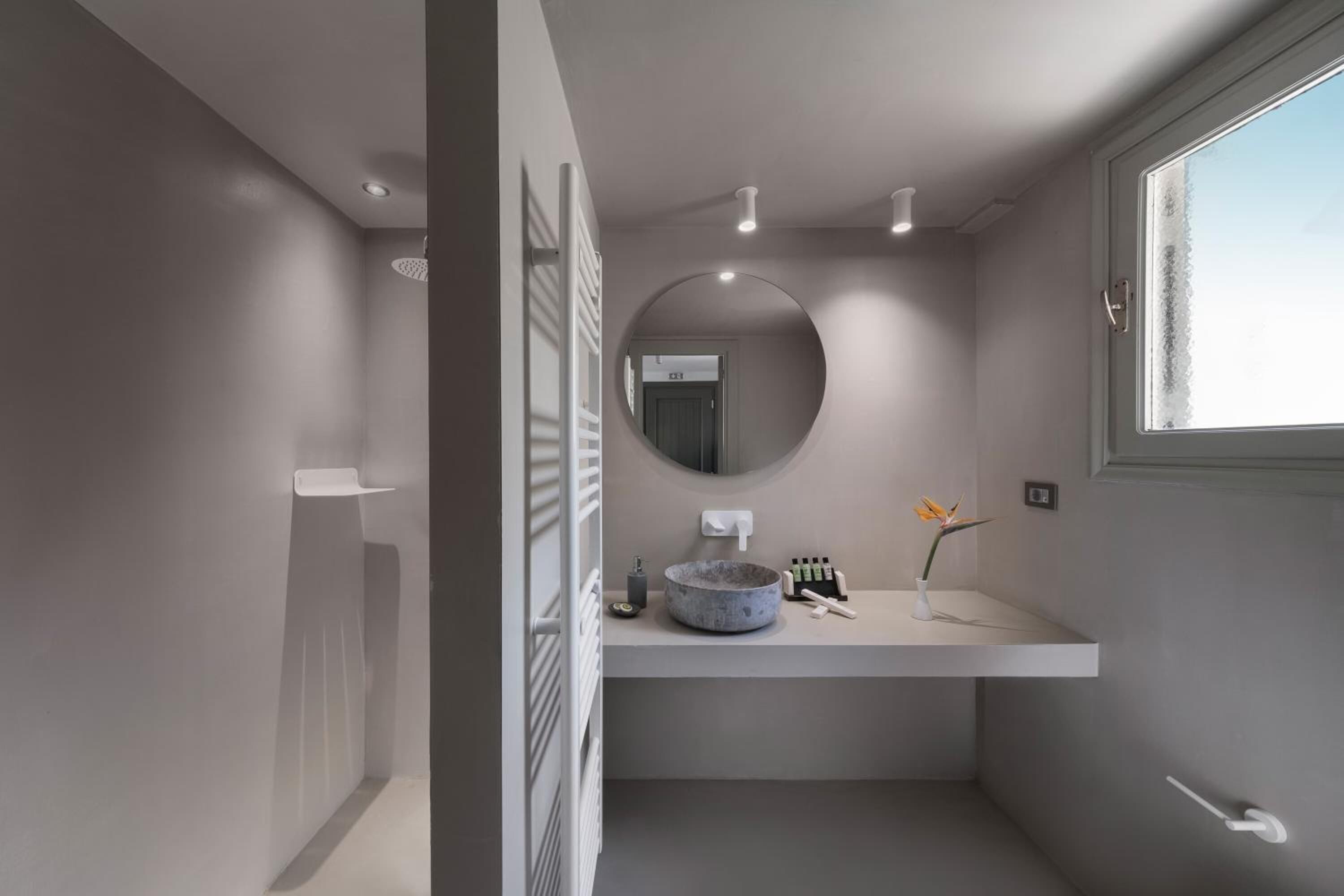 A modern bathroom with a round mirror, a sink with a bowl, and a window.