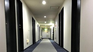 A long, narrow hotel corridor with doors on both sides, carpeted floors, and overhead lighting. - Hotel 1 2 3 Kurashiki (Kurashiki)