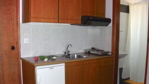 A compact kitchen with wooden cabinets, a white dishwasher, a sink, and a stove. - Iris Apartments and Rooms (Kantanos-Selino)