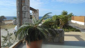 A balcony with a view of the ocean, stone pillars, and tropical plants. - Iris Apartments and Rooms (Kantanos-Selino)