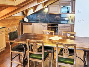 A rustic kitchen with wooden cabinets, a large wooden table, and a stone backsplash. - Edelweiss B by Interhome (Leukerbad)