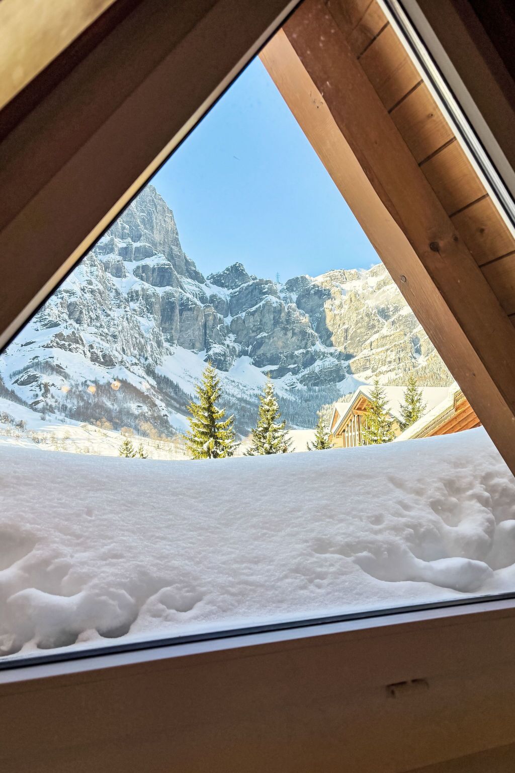 A snow-covered mountain landscape through a wooden window frame.