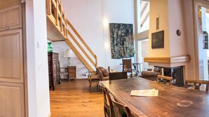 Et rummeligt spiseområde med et træbord og stole, en trappe til en etage ovenover, og en pejs.