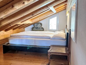 A loft bedroom with a wooden ceiling, a bed, a nightstand, and a window. - Edelweiss B by Interhome (Leukerbad)