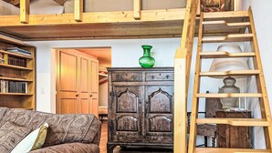 Et loftrum med synlige træbjælker, en trætrap, en grøn vase, et træskab og en sofa.
