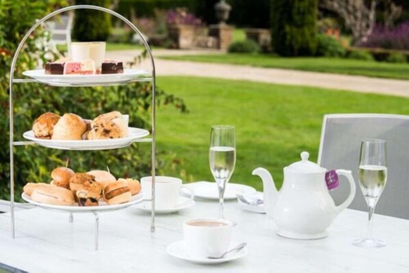 A three-tiered tea service set outdoors with pastries, a teapot, and glasses of water. - Barnett Hill (Guildford)