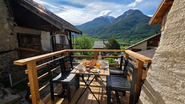 Une terrasse en bois avec une table dressée pour le petit-déjeuner, offrant une vue sur un paysage montagneux.