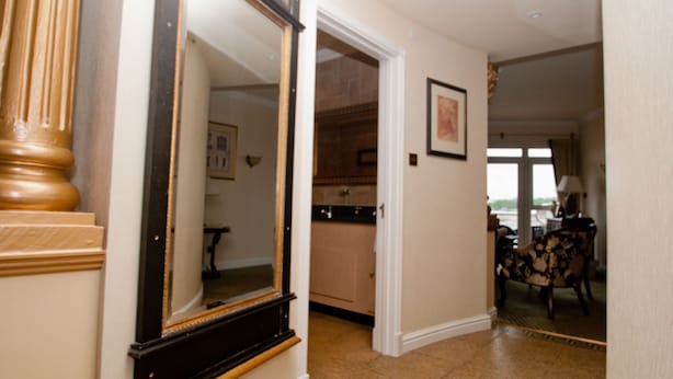A hallway with a wooden floor, a mirror, a door leading to a kitchen, and a dining area with a chair. - Little Haven Hotel (South Shields)