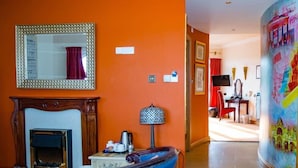 A room with an orange wall, a fireplace, a blue armchair, a lamp, and a large painting. - Little Haven Hotel (South Shields)