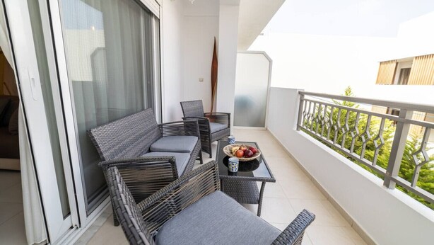 Un balcón con mobiliario de mimbre, una mesa con fruta y vistas al verdor.