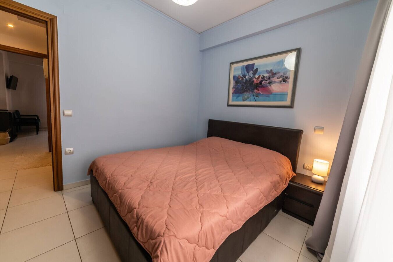 Et soveværelse med seng, et natbord, en lampe og et billede på væggen.