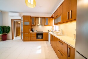 A modern kitchen with wooden cabinets, stainless steel appliances, and a large window providing natural light. - Heronissos Apartment (Limenas Chersonisou)