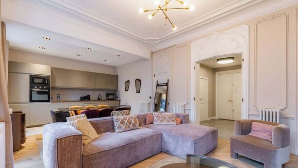 A modern living room with a sectional sofa, a glass coffee table, and a kitchen in the background. - Prestige Haussmannien & AC - Madeleine Paris 8 (Paris)