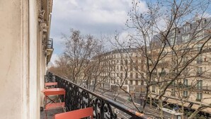 A balcony with red chairs and a wrought iron railing overlooking a street with buildings and bare trees. - Prestige Haussmannien & AC - Madeleine Paris 8 (Paris)