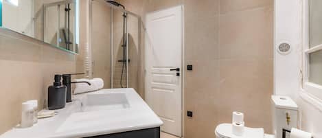 Een moderne badkamer met een douchecabine van glas, een wit toilet en een wastafel met spiegel.