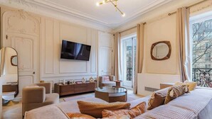 A spacious living room with a large sofa, a coffee table, and a flat-screen TV mounted on the wall. - Prestige Haussmannien & AC - Madeleine Paris 8 (Paris)