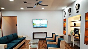 A modern hotel lobby with a sofa set, a TV mounted on the wall, a desk with a computer, and a ceiling fan. - Garden Inn Airport (Auckland)
