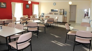A dining area with tables and chairs, a kitchen in the background, and a red wall. - Motel 359 (Tamworth)