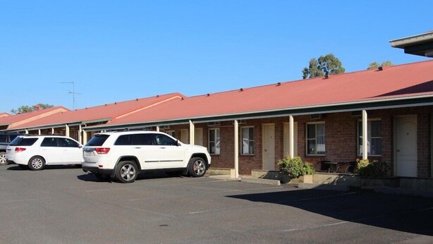 A row of motel rooms with a red roof, a parking lot, and two white SUVs parked in front. - Motel 359 (Tamworth)