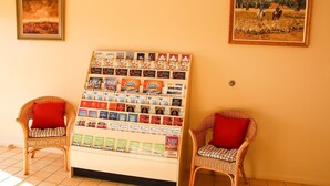 A room with two wicker chairs with red cushions, a bulletin board with travel brochures, and two framed pictures on the wall. - Motel 359 (Tamworth)