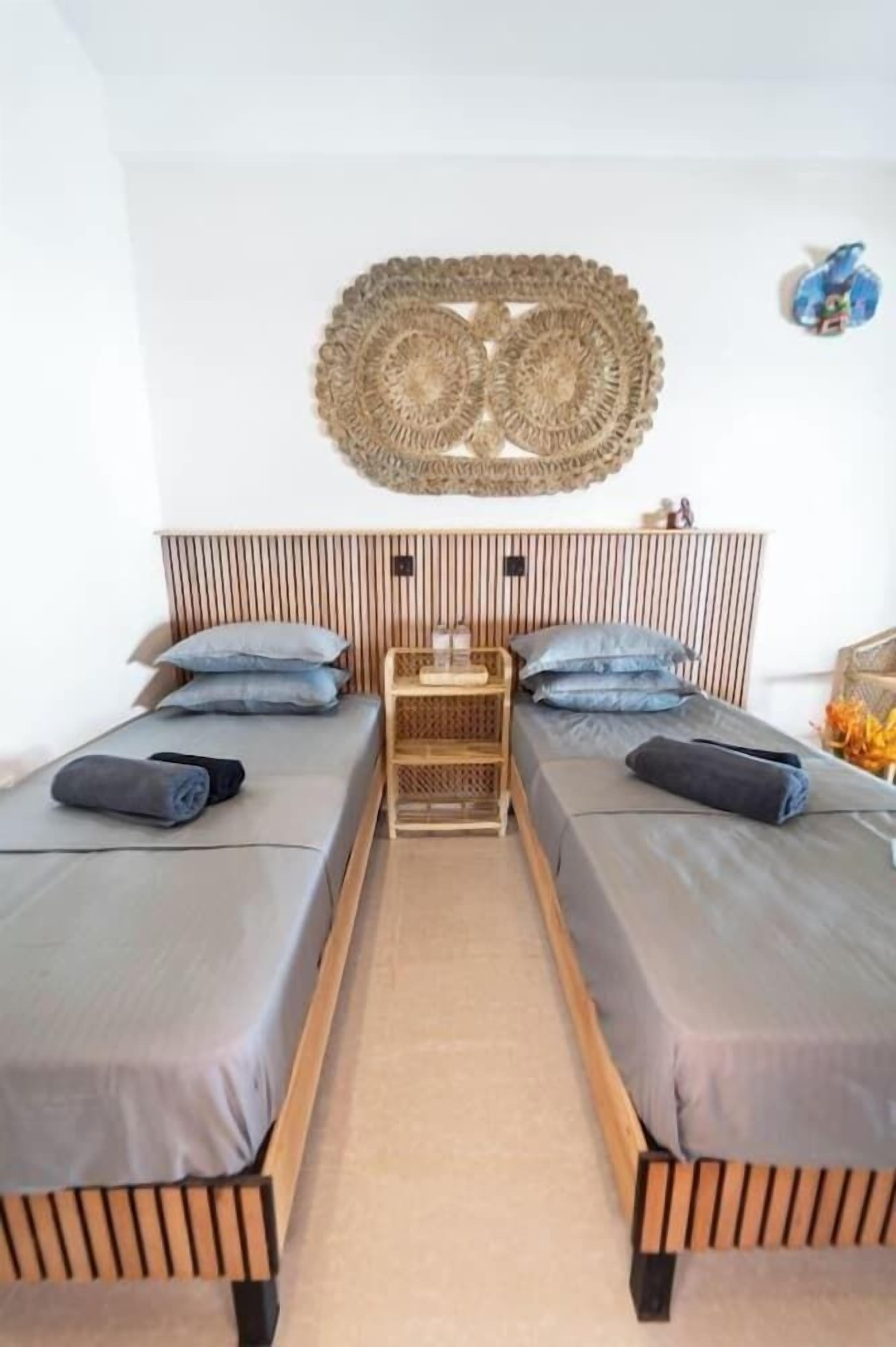 A room with two beds, a woven headboard, and a small wooden side table.