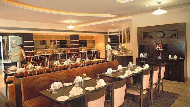 A restaurant with a long counter, multiple tables, and a bar area. - Lemon Tree Hotel Baddi (Baddi)