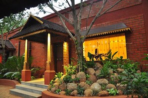 A traditional building with a tiled roof, brick walls, and a wooden porch with steps leading to a door. - Aalankrita Resort AND Convention (Shamirpet)