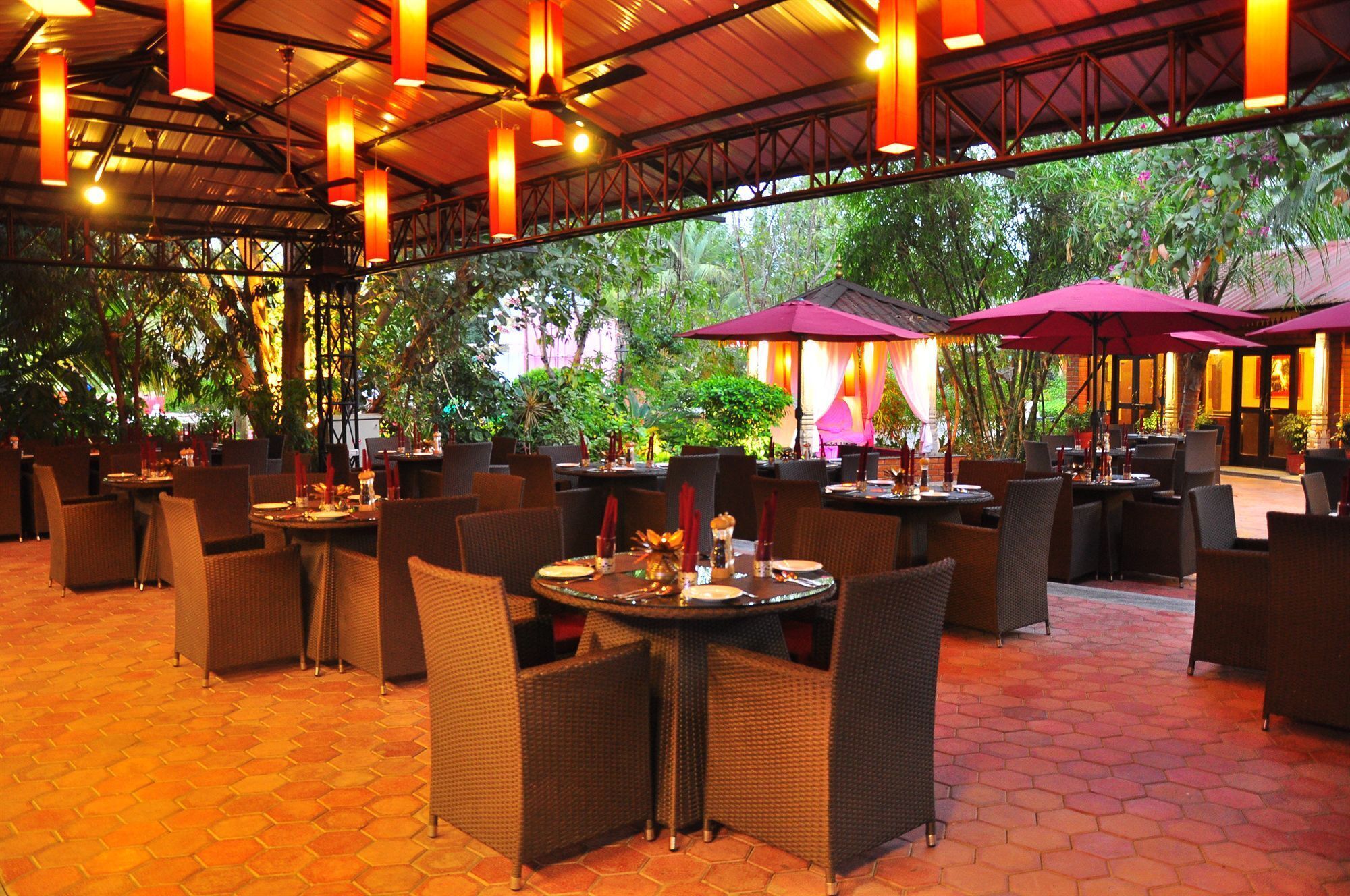 An outdoor restaurant with hexagonal tiled flooring, wicker furniture, and red umbrellas.