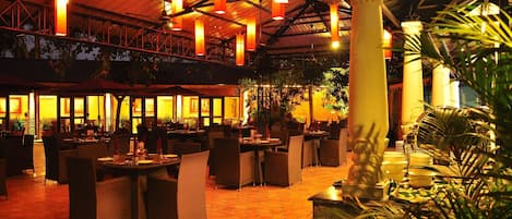 Un restaurante interior con suelo de diseño hexagonal, mobiliario de mimbre y colgantes de luz naranja.