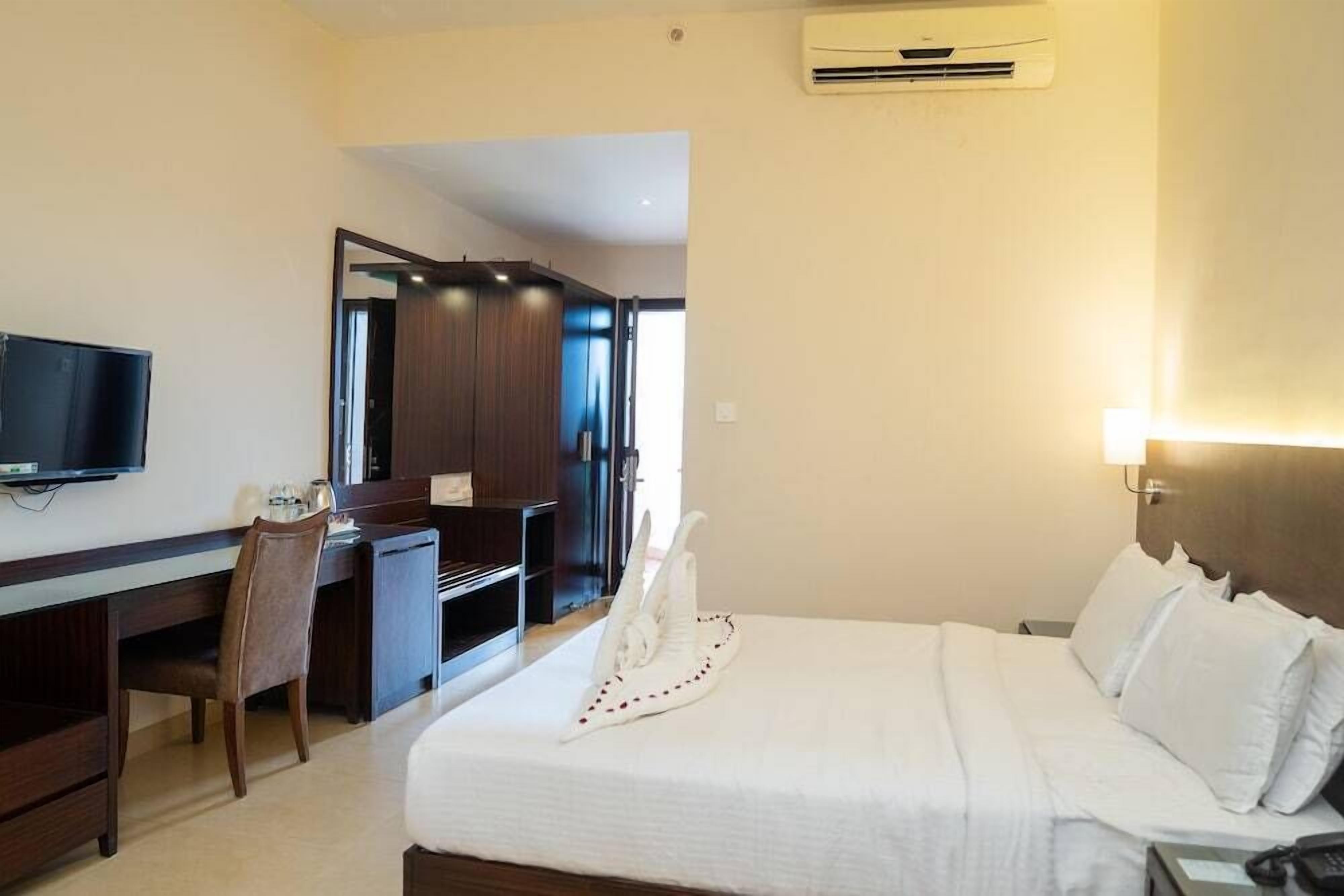A hotel room with a bed, a desk, a chair, a television, and an air conditioning unit.