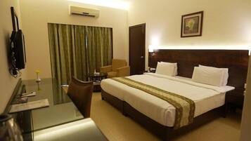 A hotel room with a bed, a desk with a chair, a telephone, and a window with curtains.