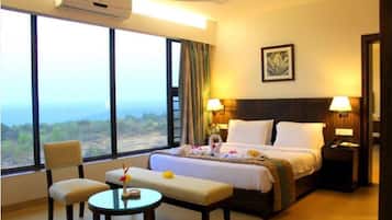 A hotel room with a large window, a bed, a bedside table, a chair, and a small table with a vase.
