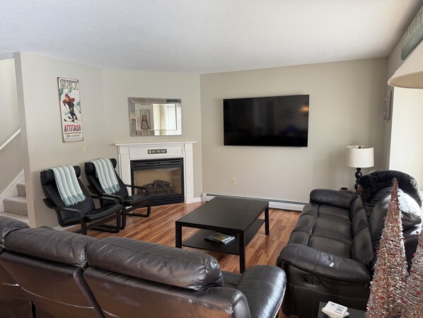 A living room with a fireplace, a TV, leather sofas, and a coffee table. - Spacious 4BR Retreat/ Short Walk To Saco River/Prime Location (Bartlett)
