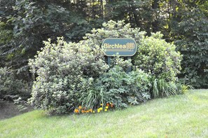 A sign reading "Birchlea" surrounded by dense foliage and a grassy area.