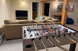 A living room with a foosball table, a beige sofa, a television, and a wooden door.