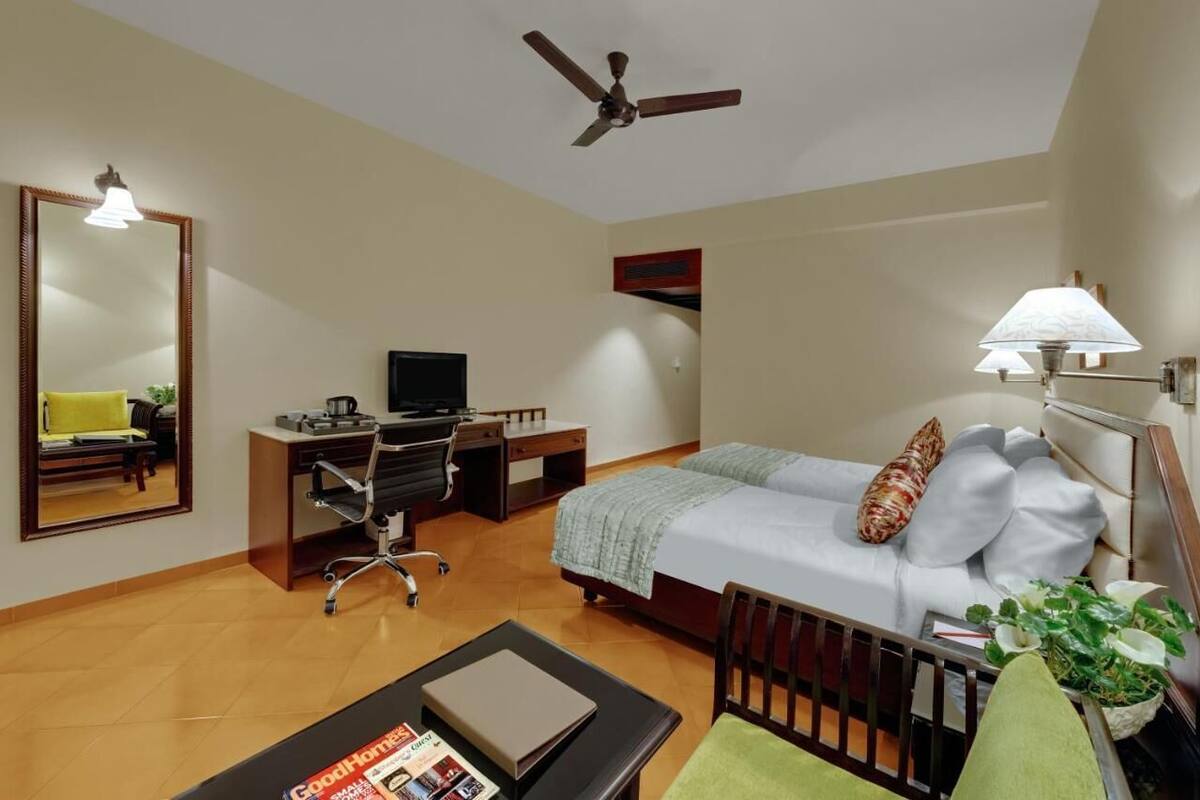 A bedroom with a bed, desk, chair, television, and a ceiling fan.