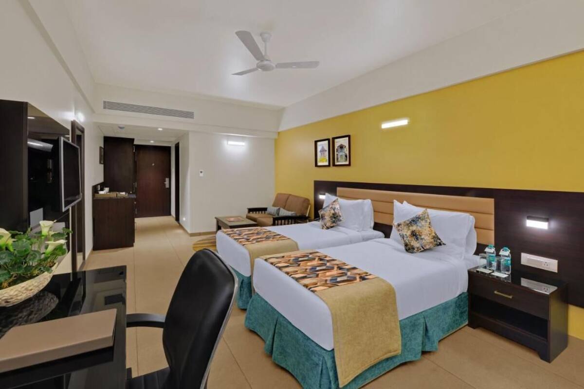 A hotel room with two beds, a desk with a computer, a chair, a TV, and a ceiling fan.