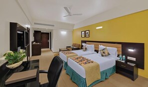 A hotel room with two beds, a desk with a computer, a chair, a TV, and a ceiling fan. - The Fern Kesarval Hotel & Spa Verna Plateau, Goa (Verna)