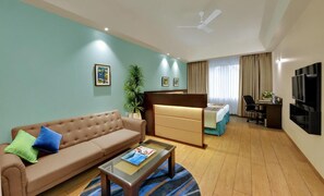 Ein Hotelzimmer mit einer Couch, einem Bett, einem Schreibtisch, einem Fernseher und einem Deckenventilator.