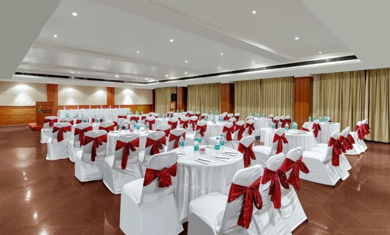 A conference room with round tables, white chairs, and red sashes.