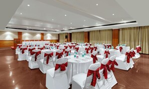 Een vergaderzaal met ronde tafels, witte stoelen en rode linten.