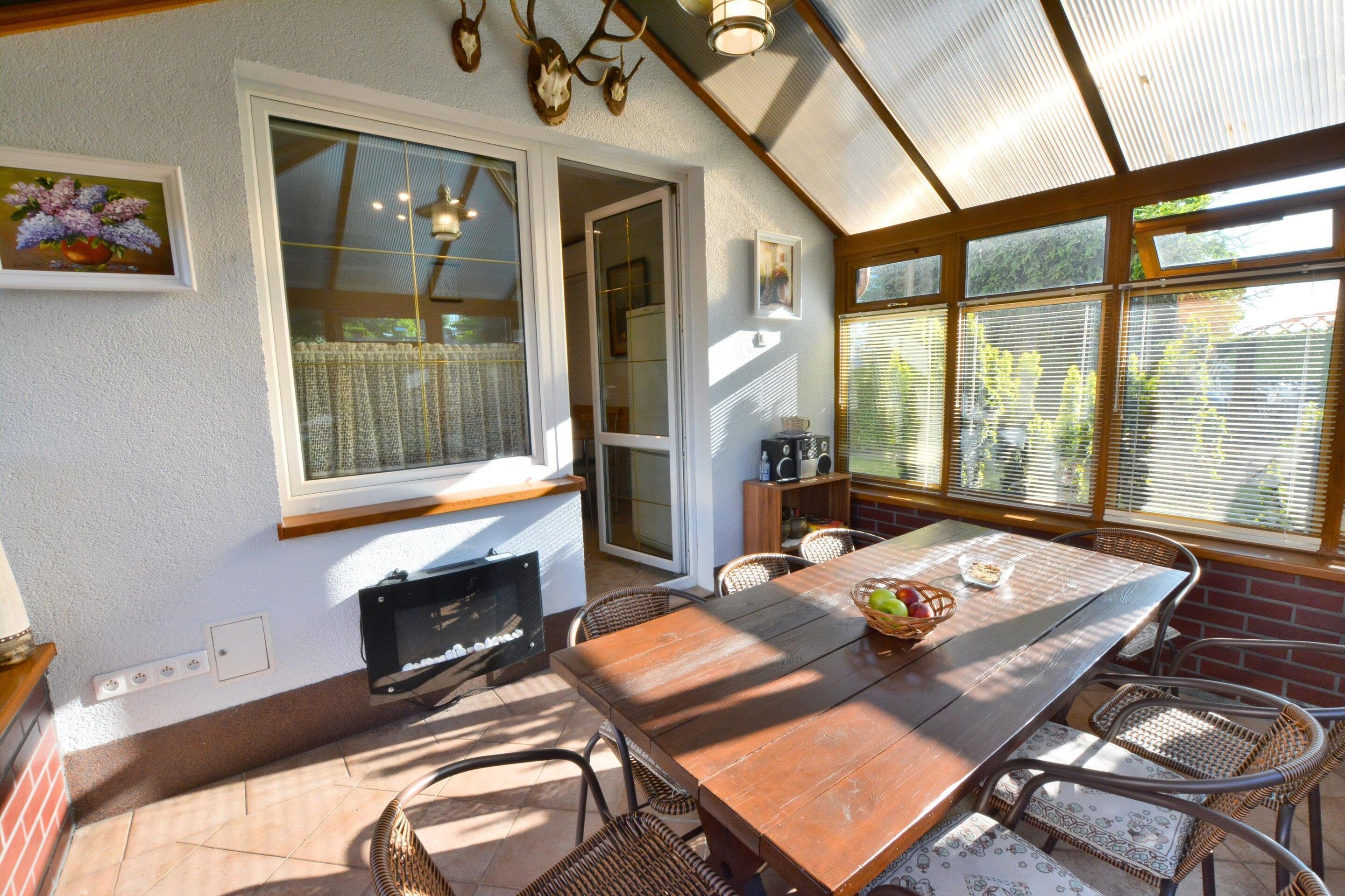 Un coin repas baigné de lumière naturelle, avec une table en bois, des chaises en osier et une vue sur la verdure grâce à de grandes fenêtres.